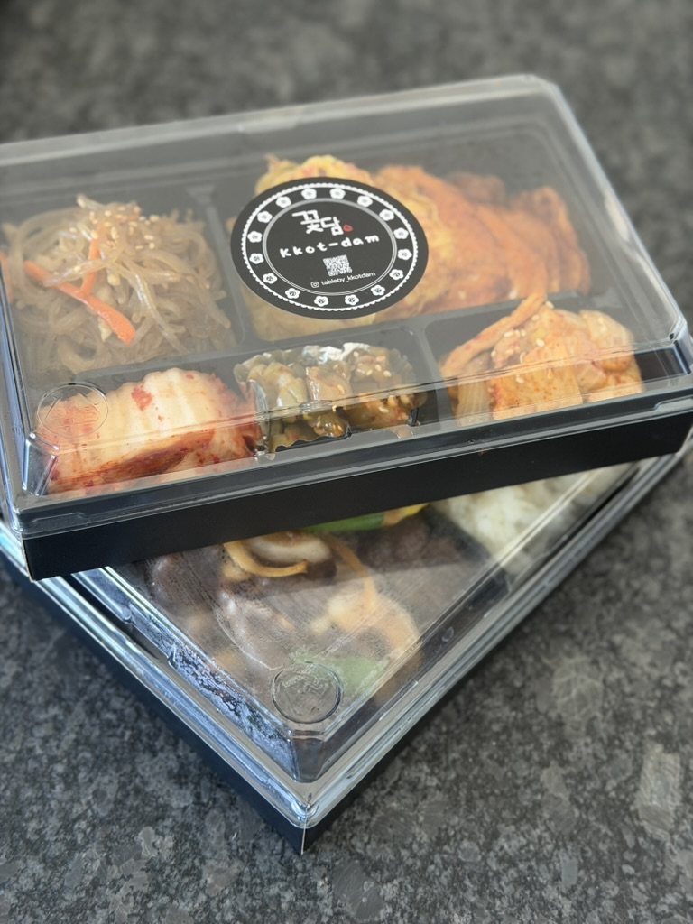 Two sealed Kkot-dam lunchboxes stacked, with the Kkot-dam sticker on the lid