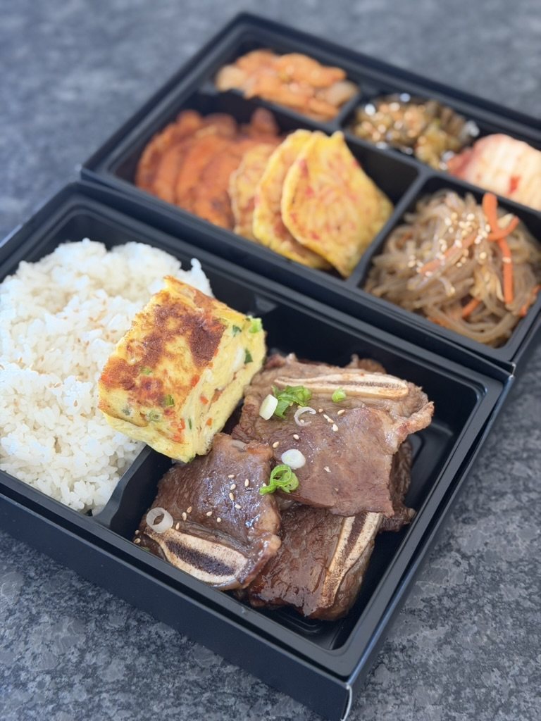 Galbi lunchbox with rice, egg roll and a tier of banchan